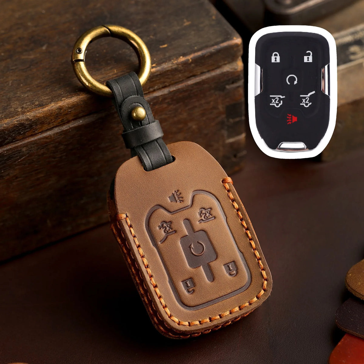 A brown leather key cover with a brass ring attached, featuring embossed symbols for Chevrolet and GMC trucks.