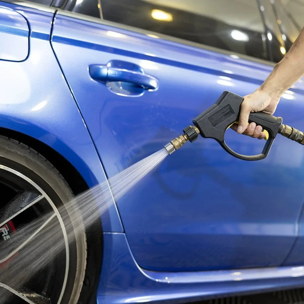 A hand sprays water from a high-pressure shower head nozzle onto the blue paint of a car.