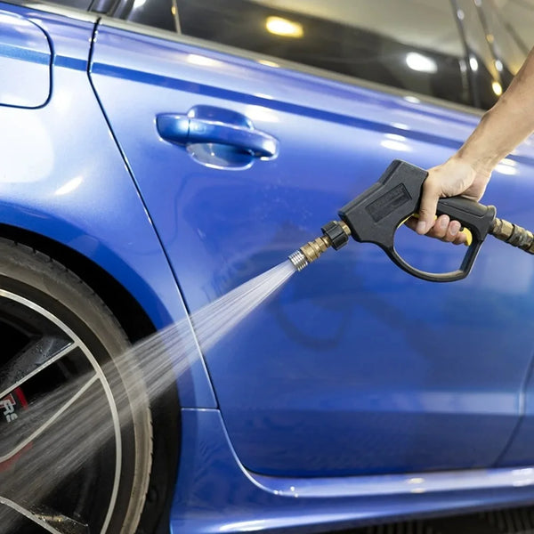 A hand sprays water from a high-pressure shower head nozzle onto the blue paint of a car.