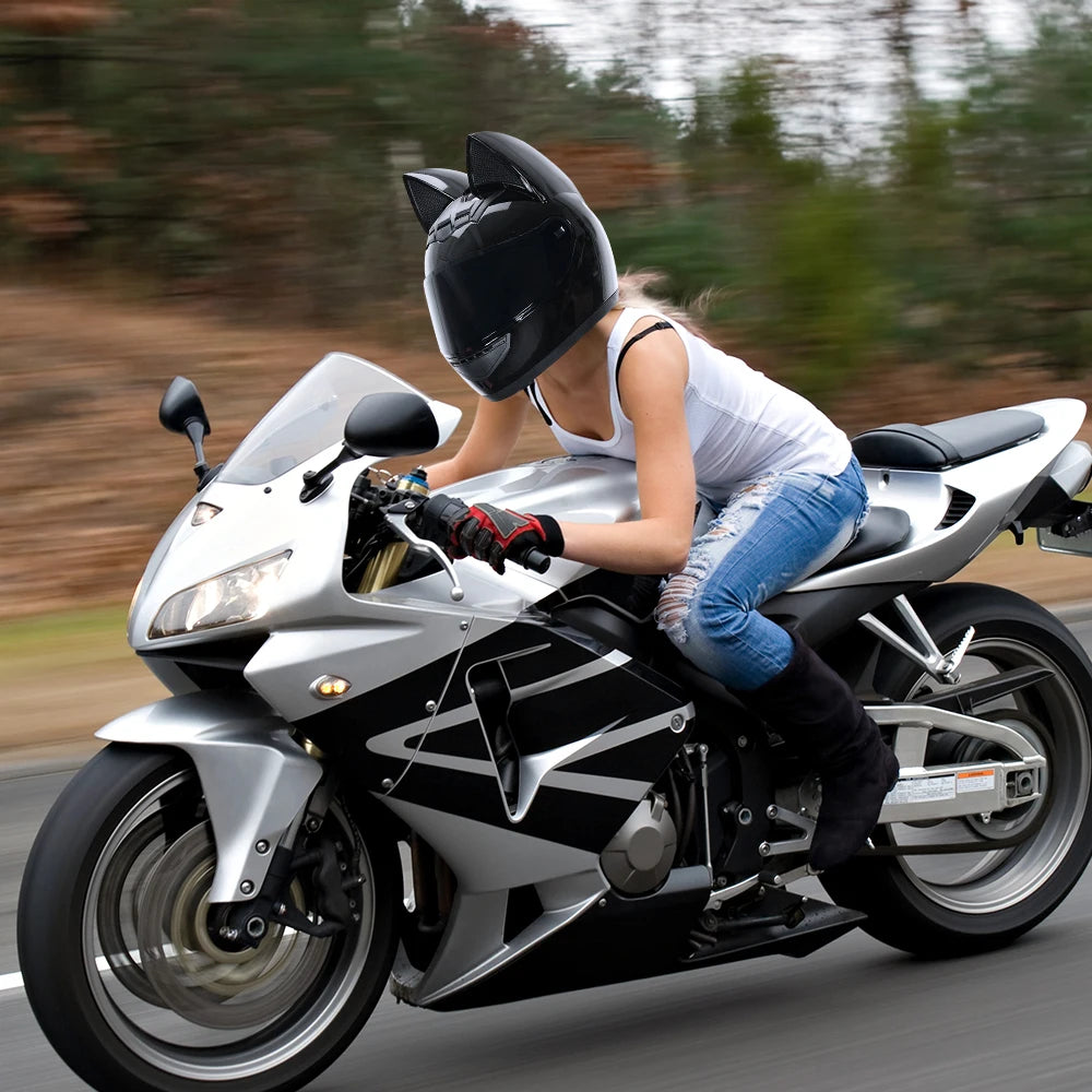 A person wearing a black full face motorcycle helmet rides a silver and black sport bike on a road.
