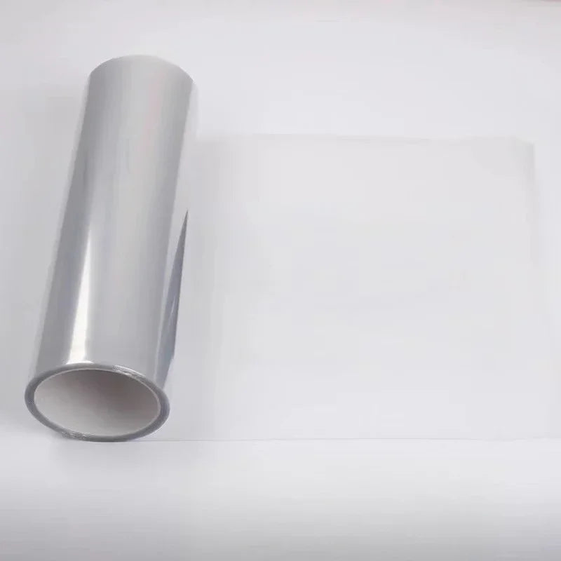A roll of clear tint film for car headlights and taillights lying on a white surface.