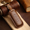 A brown leather car key fob cover attached to a coiled leather cord, resting on a wooden surface.