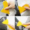 A hand is using a yellow vinyl wrapping tool to apply a film to a car surface.