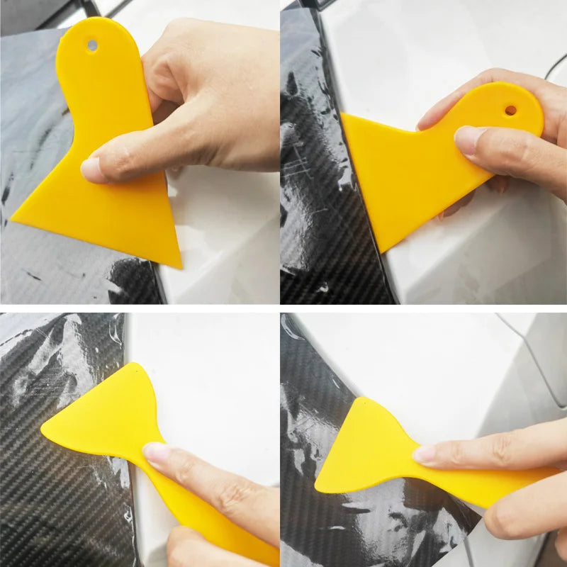 A hand is using a yellow vinyl wrapping tool to apply a film to a car surface.