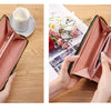 A pink leather long wallet with a black trim is shown open, next to a cup and saucer.