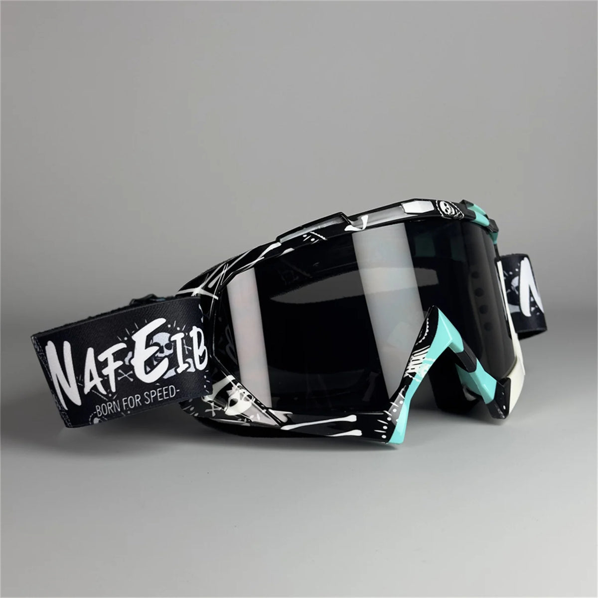 Un par de gafas de motocicleta negras con detalles blancos y turquesa sobre una superficie gris.