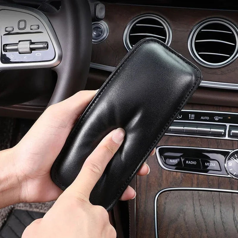 A hand holds a black leather knee pad product in the context of a car interior.