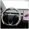 A close-up view of a black steering wheel with a light beige breathable perforated leather cover.