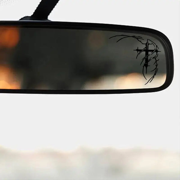 A close-up of a black car mirror with a gothic thorn cross decal on the surface.