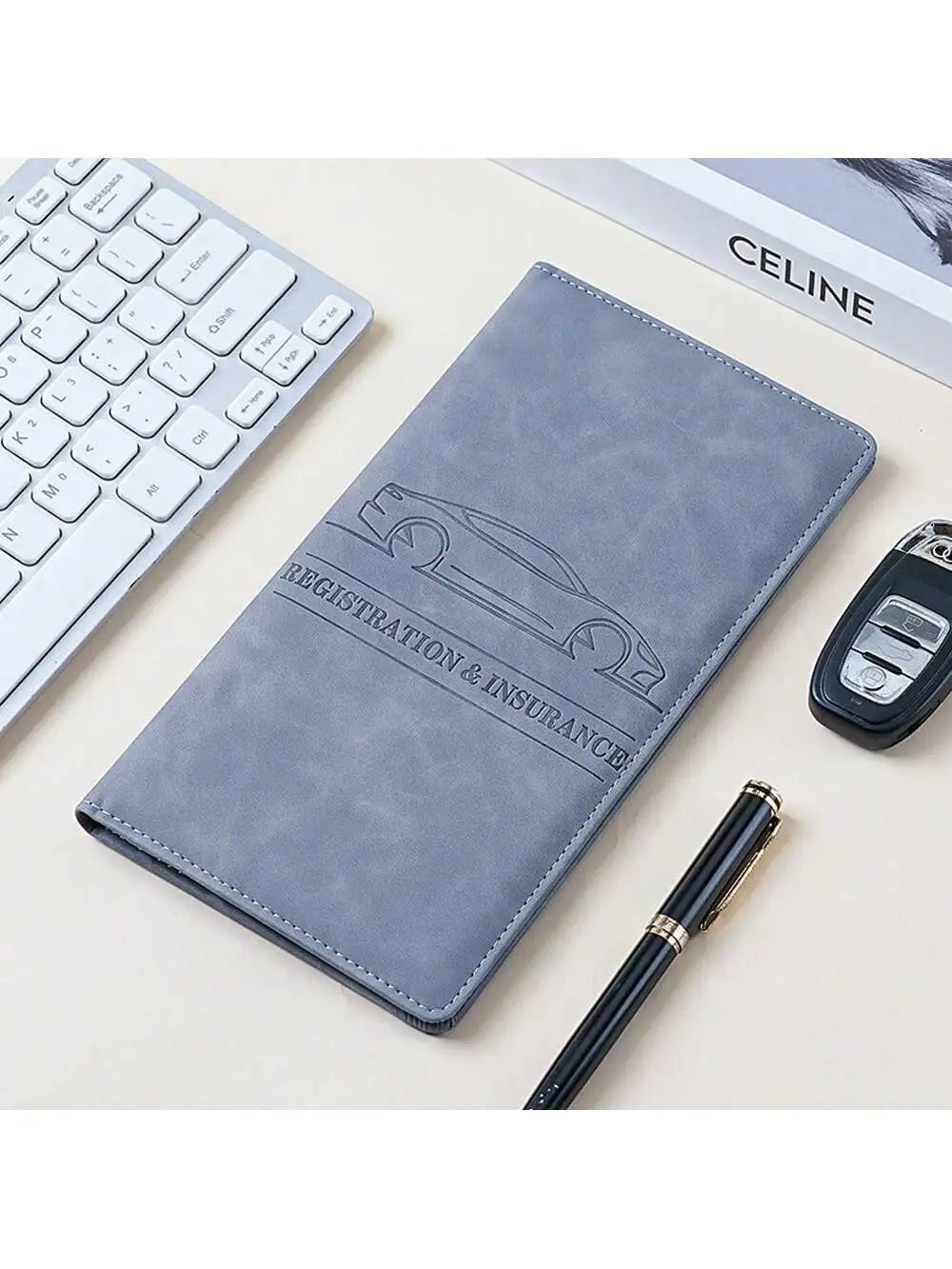 Graues Lederdokumentenhalter mit Autosilhouette, neben einer weißen Tastatur und einem Stift.