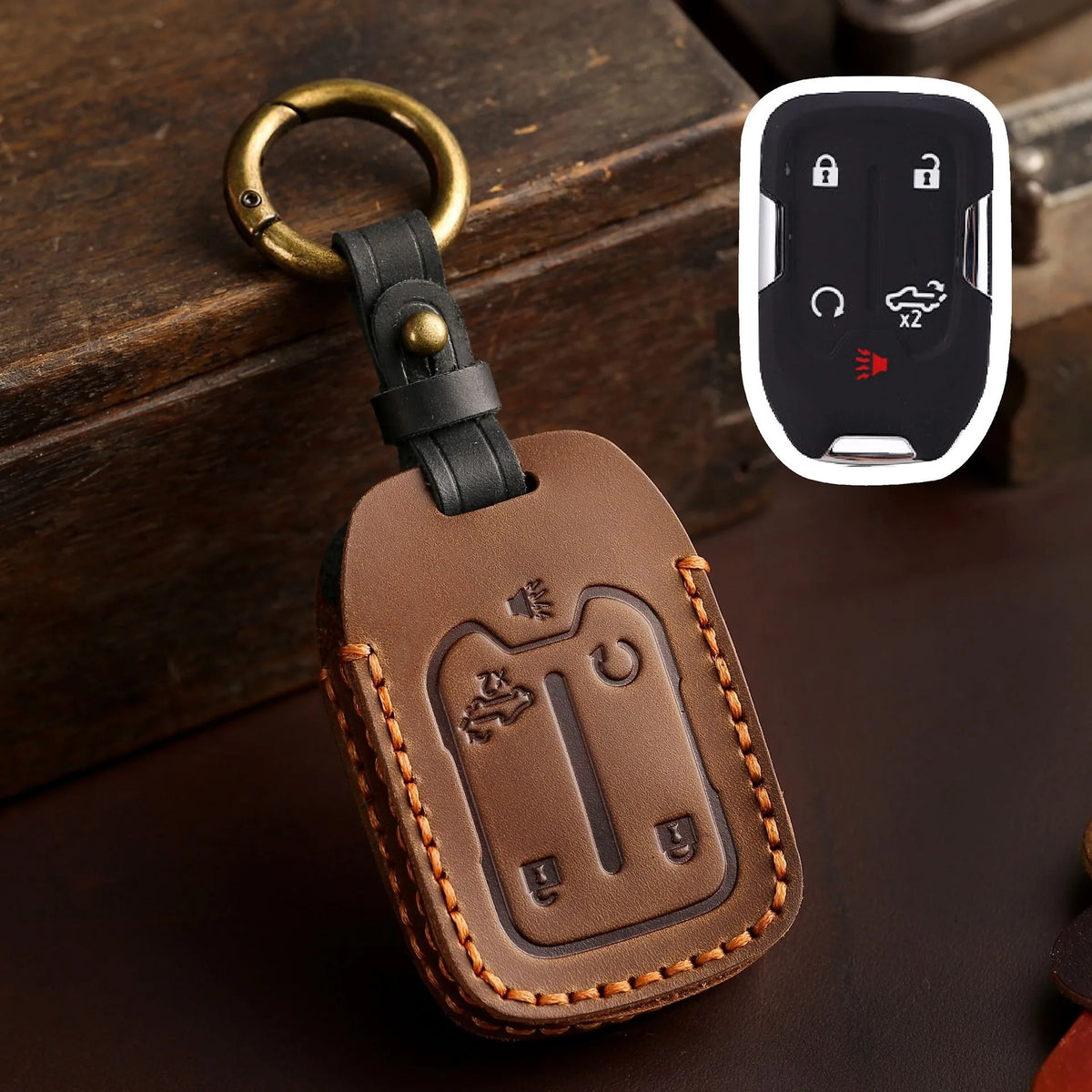 A brown leather key cover with a brass ring and a black strap, featuring cutouts for Chevrolet and GMC truck keys.
