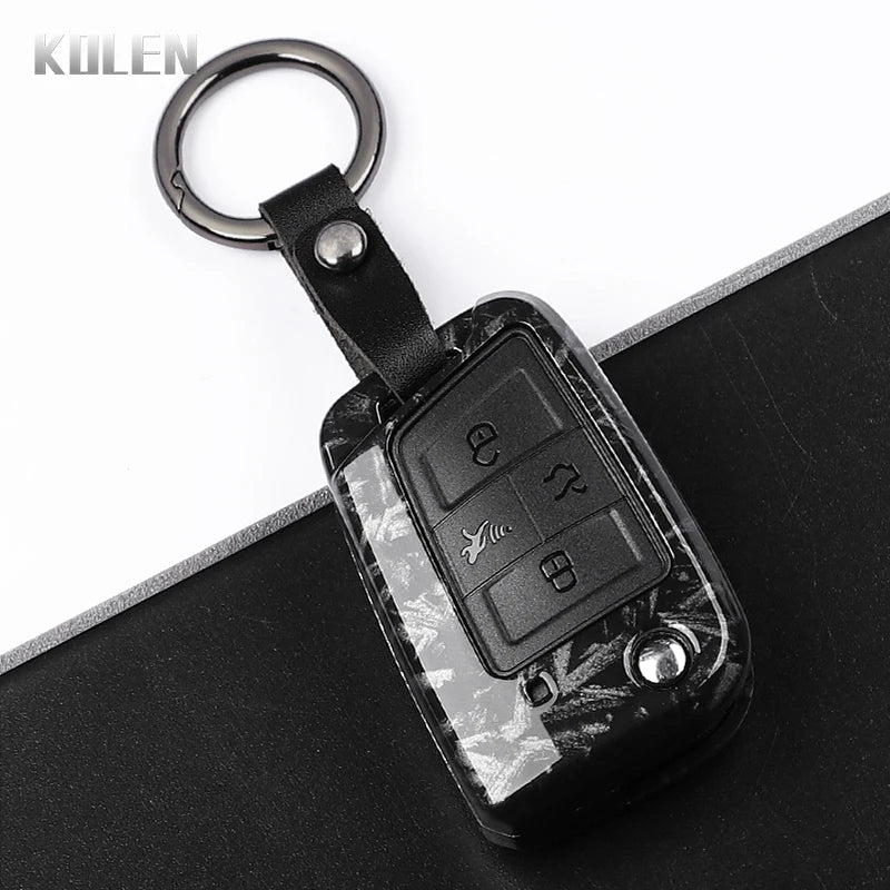 A black carbon fiber button cover for a car key, attached to a metal keyring.