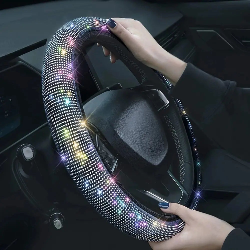A hand is gripping a black steering wheel covered in sparkling rhinestones.