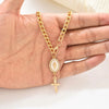 A gold chain necklace with a decorative oval pendant and a cross charm is held in a person's hand.