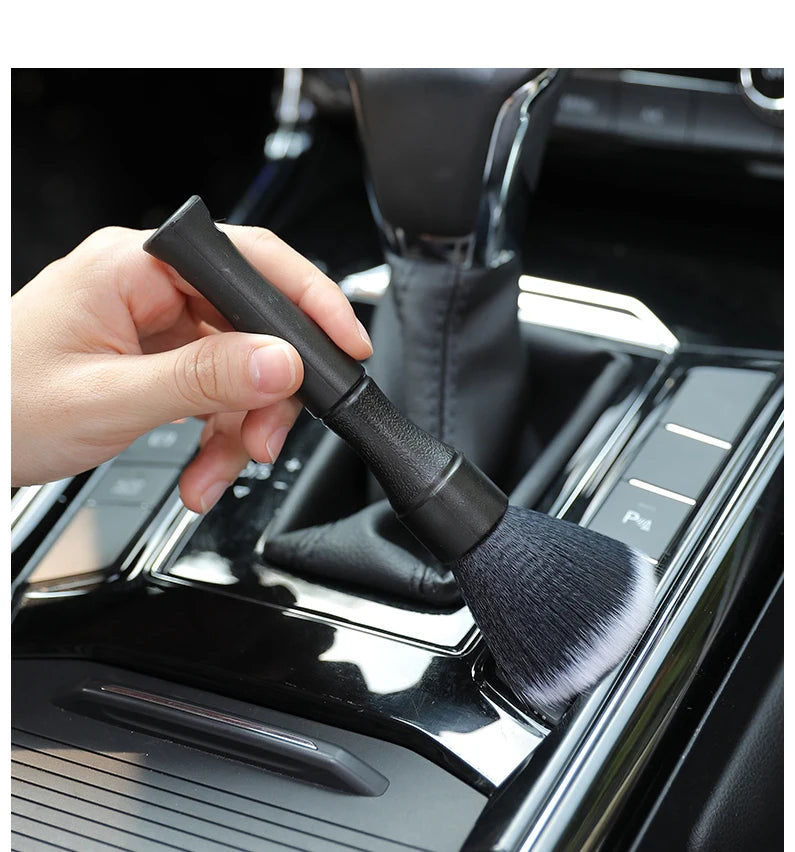 Une main tient une brosse de detailing noire à poils doux, positionnée sur la surface de l'intérieur d'une voiture.