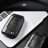 A close-up view of a black carbon fiber button cover for a car key resting on a white laptop.