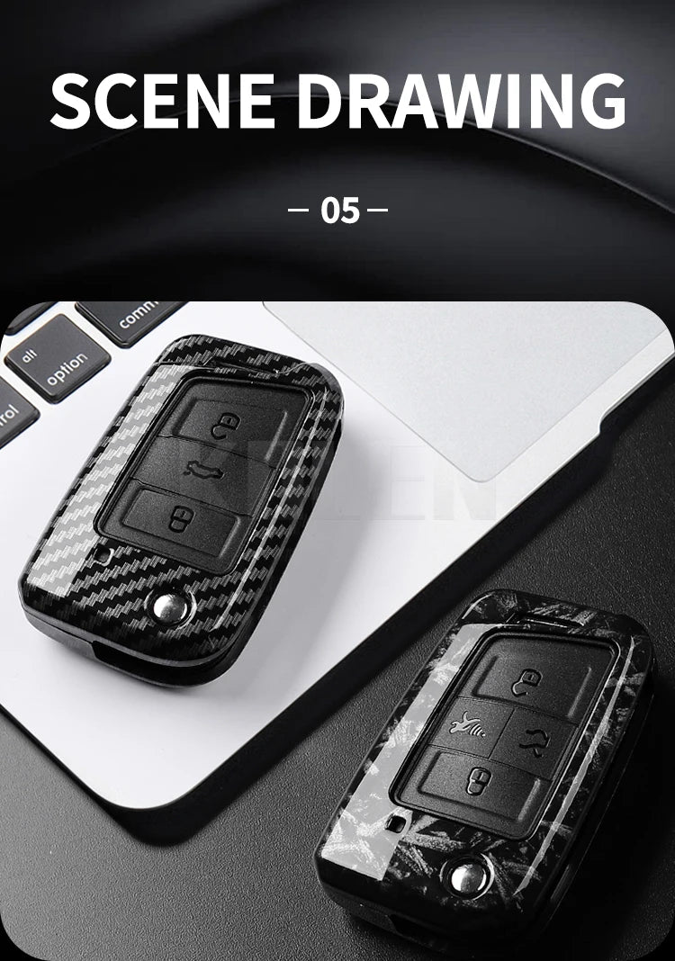 A close-up view of a black carbon fiber button cover for a car key resting on a white laptop.