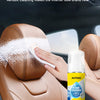A hand is applying foam cleaner to a brown car interior seat, demonstrating the product's cleaning ability.