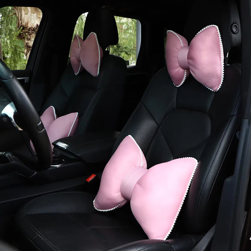 Pink ergonomic car headrest pillow with a bow design shown in the back seat of a car.