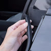 A hand is pressing a black rubber seal strip, a universal car door edge weatherstrip, into the B-pillar of a vehicle.