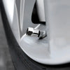 A close-up view of a silver tire valve cap being installed on a white automotive wheel rim.
