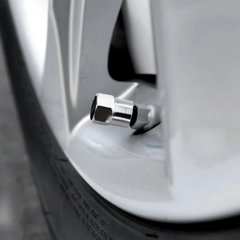 A close-up view of a silver tire valve cap being installed on a white automotive wheel rim.