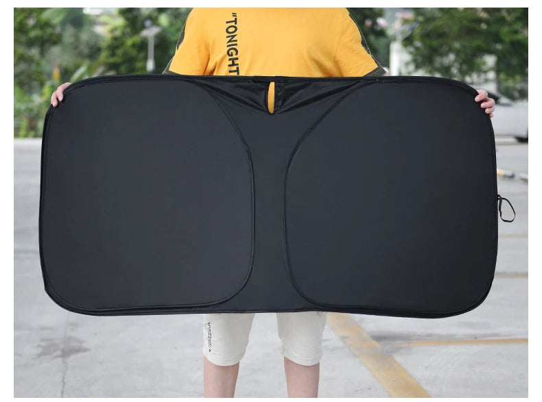 Un pare-soleil noir de voiture premium est tenu par une personne sur un fond extérieur lumineux.