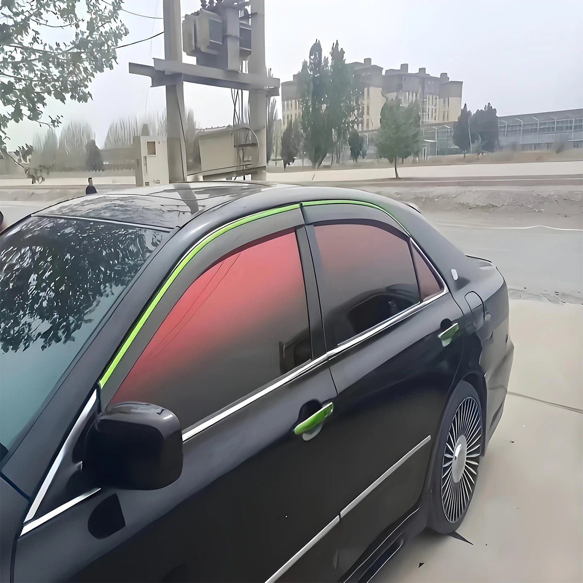 A close-up view of a black car with a tinted window, showing the installation or effect of color changing solar tint film.