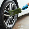 A hand using a black brush to clean the wheel of a car with soapy water.