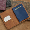 A brown leather passport holder with a navy blue passport and a white ID card resting on a wooden surface.