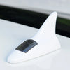 A white solar car antenna with a shark fin design resting on a white surface.