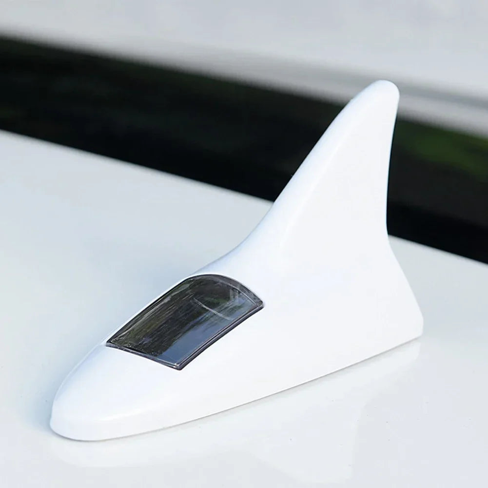 A white solar car antenna with a shark fin design resting on a white surface.