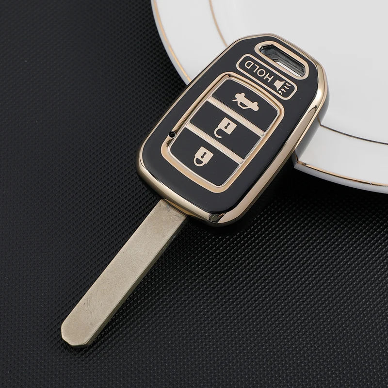 A close-up of a black and gold TPU car key fob cover with a metal blade resting on a white surface.