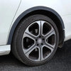 A close-up view of a car wheel with a black rim and tire, showing the carbon fiber trim around the arch.