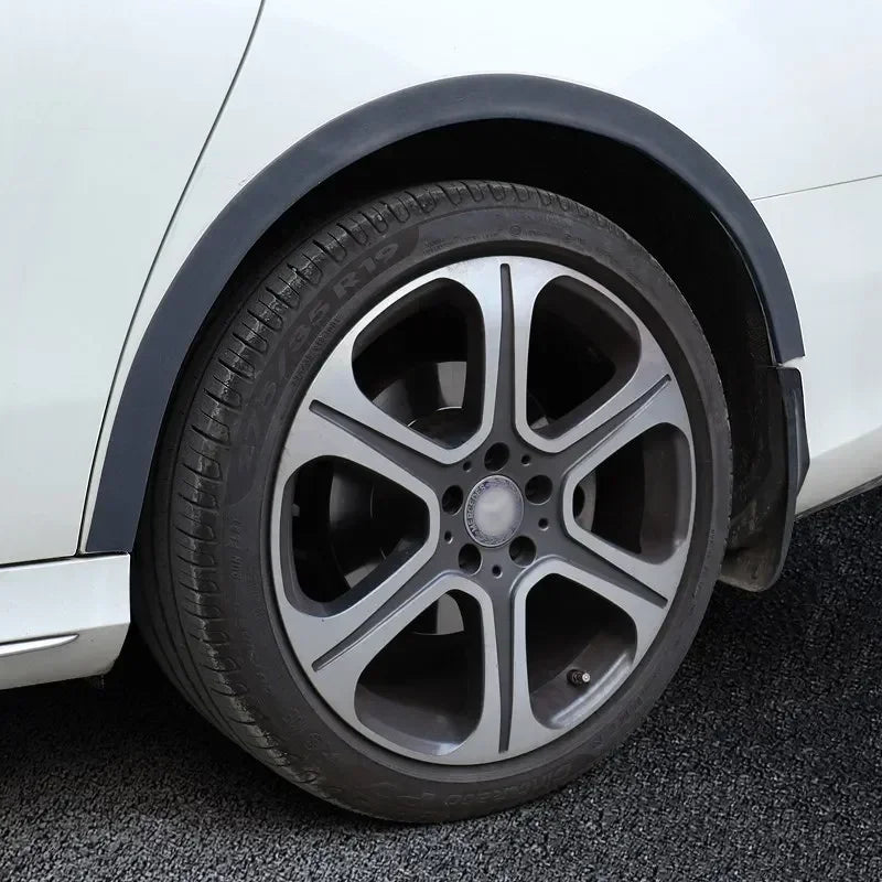 A close-up view of a car wheel with a black rim and tire, showing the carbon fiber trim around the arch.