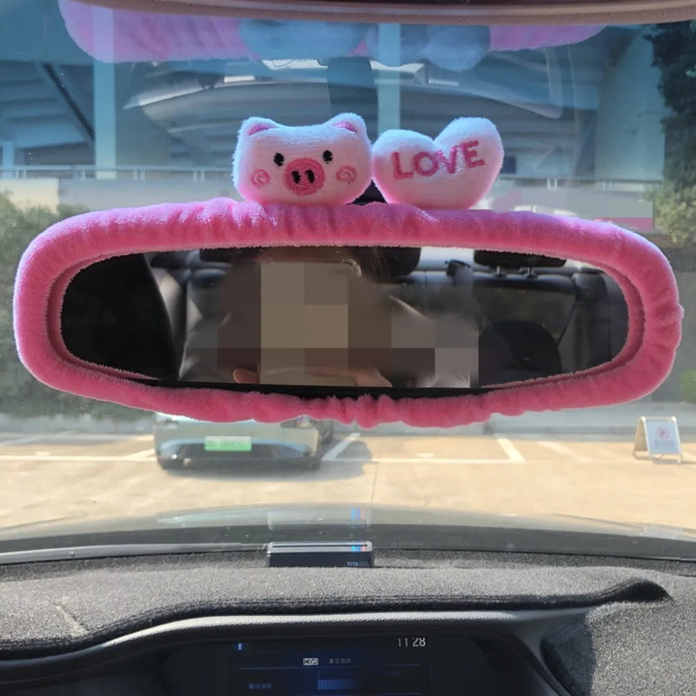 A pink cartoon pig plush is placed on a rearview mirror cover inside a car.