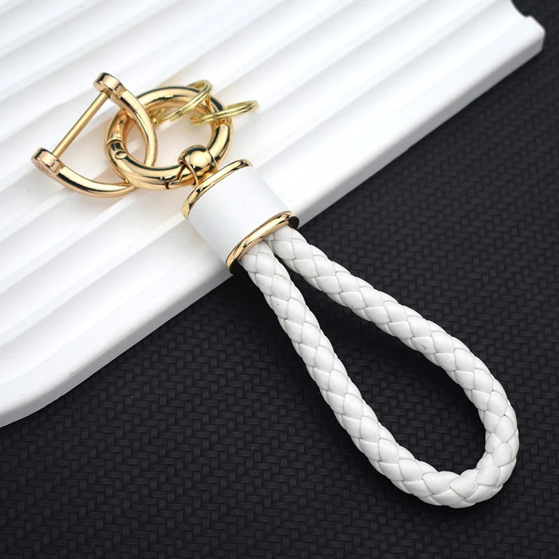 Gold-toned TPU car key fob cover with a white braided lanyard resting on a black surface.