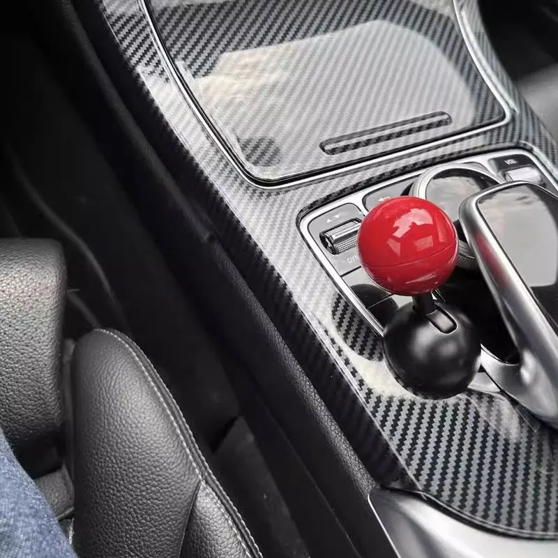 Close-up of a push start ignition button cover on a car dashboard with carbon fiber trim.