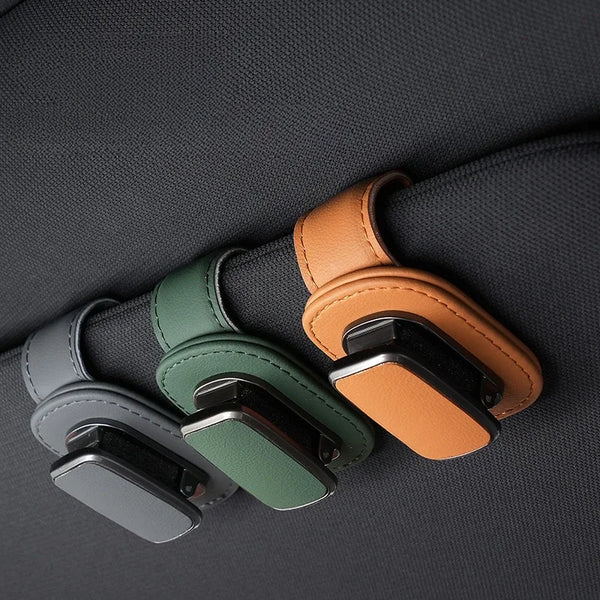 A set of PU leather eyeglass storage clips in olive green and tan colors resting on a dark gray fabric.