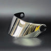 Visor de casco de motocicleta plateado con correa negra, reflejando luz en una superficie oscura.