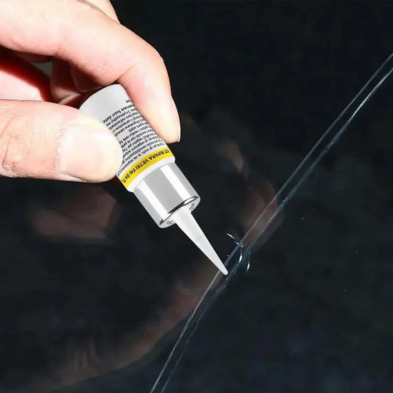 A hand holds a glass tube of automotive windshield crack repair kit against a dark surface.