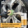 A hand is using a green brush to clean a wheel with yellow liquid foam from a bottle of wheel cleaner.