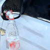 A clear plastic bottle containing a red liquid is attached to a car's rearview mirror.