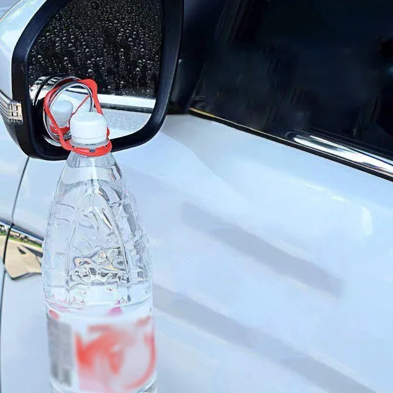 A clear plastic bottle containing a red liquid is attached to a car's rearview mirror.