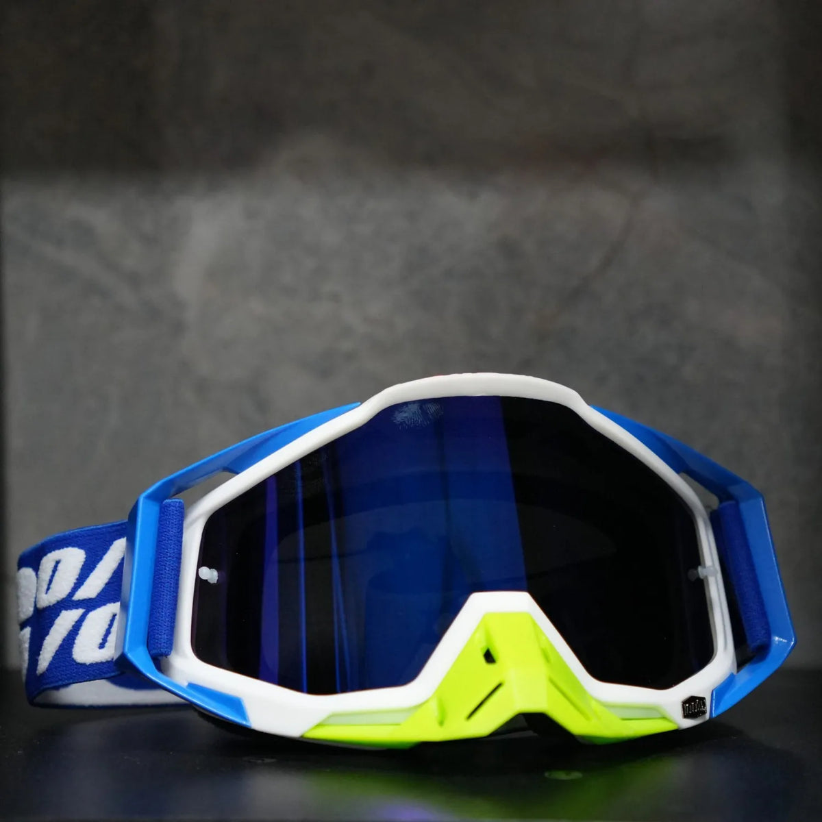 A pair of blue and white high-performance motocross goggles resting on a dark surface.