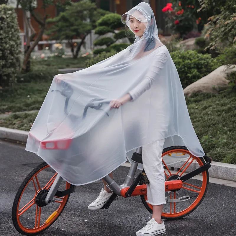 A woman wearing a transparent windproof motorcycle rain poncho rides a bicycle on a street.