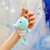 A hand holds a light blue plush bunny keychain with a gold ring against a soft, light blue background.