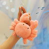 A hand holds a fluffy peach-colored plush bunny keychain with a gold ring against a light blue background.