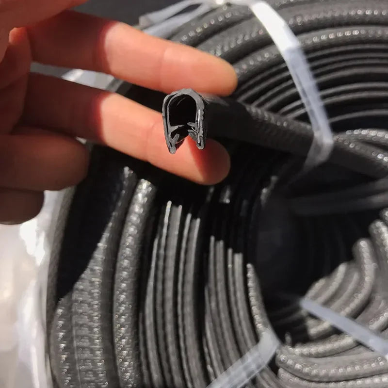 A hand holds a rubber edge seal trim for vehicle doors and windows, showing its profile against a roll of black trim.
