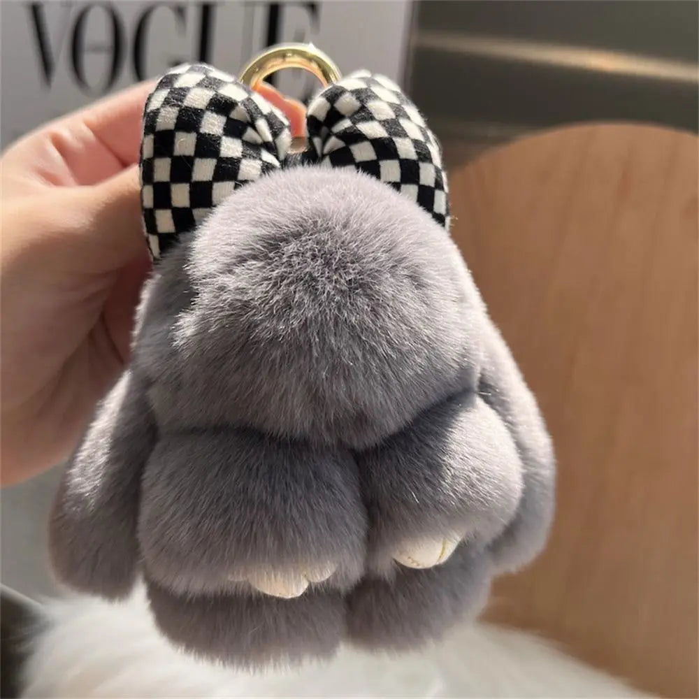 A close-up of a gray plush bunny keychain with soft fur and black and white checkered ears attached to a gold ring.
